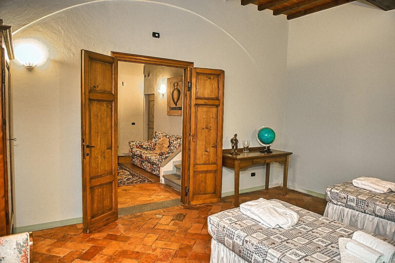 Ein Zimmer mit Holztür, einer Couch, einem Tisch mit Globus und zwei Betten mit Handtüchern.