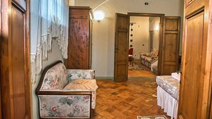 A room with a wooden floor, a floral sofa, a bed with a patterned bedspread, and a wooden wardrobe. - Apartment 'Holiday Home In Tuscany' with Mountain View, Private Terrace and Wi-Fi (Castelfiorentino)