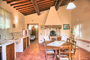 Uma cozinha rústica com teto de madeira, uma área de jantar com mesa e cadeiras, e uma lareira.