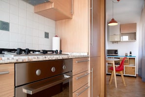 A kitchen with a stove, oven, and microwave. There is a red chair and a table with a lamp. - Holiday Home 'La Piazzetta' with Mountain View and Wi-Fi (Germignaga)