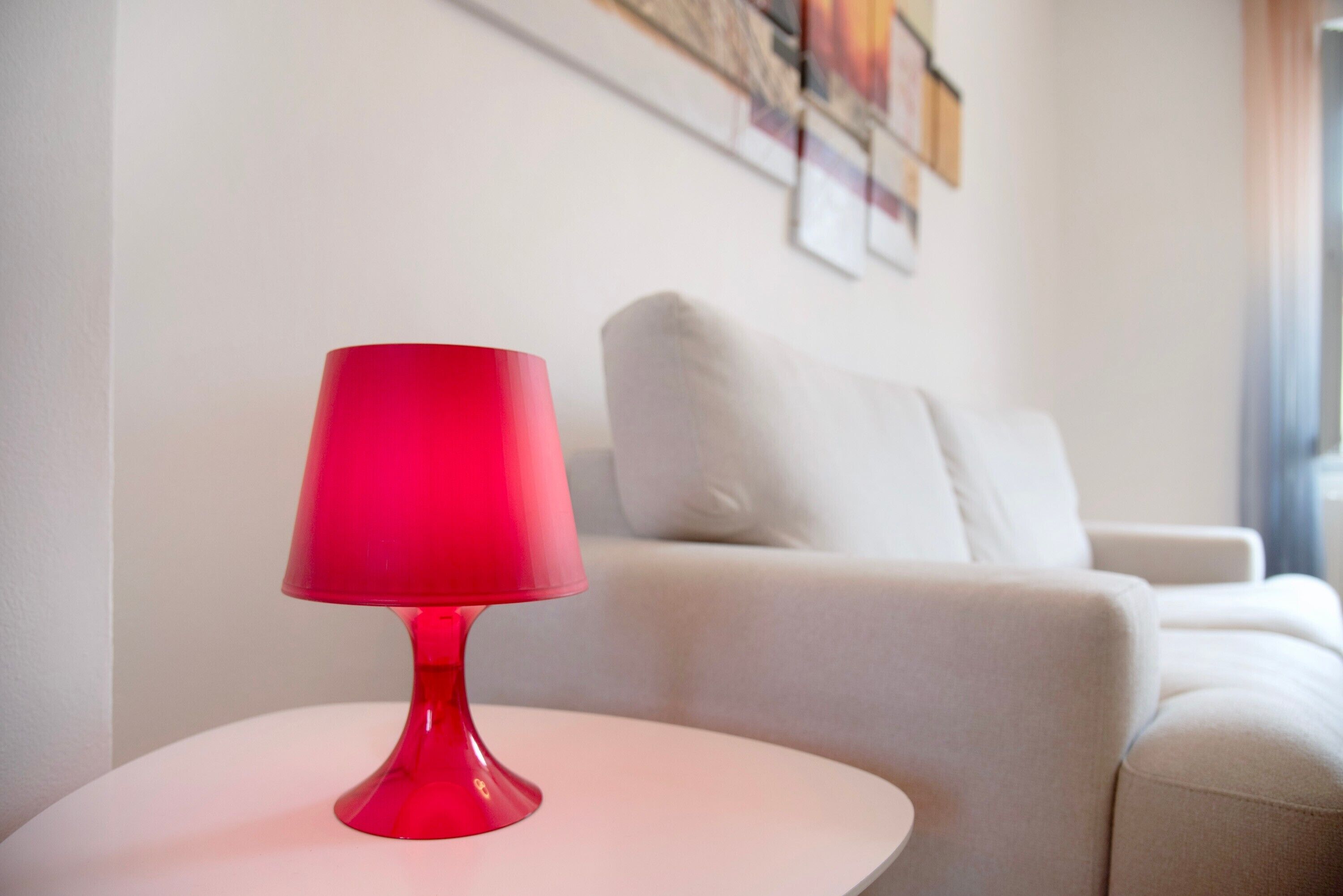 Eine rote Tischlampe steht auf einem weißen Tisch in einem Wohnzimmer mit einem weißen Sofa und einem Bild an der Wand.