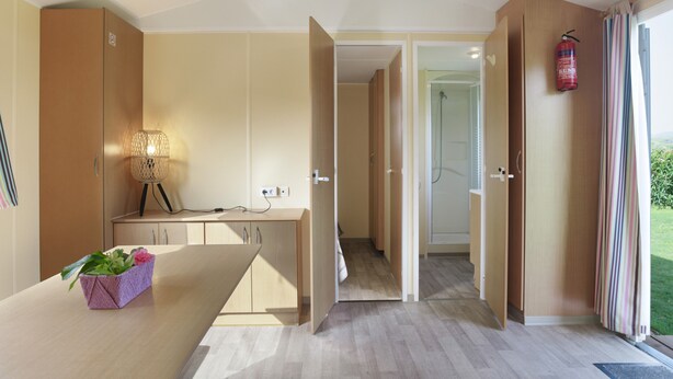Una habitación de hotel moderna con un escritorio de madera, una planta, un extintor y vistas al exterior.