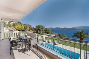 A balcony with a table and chairs, a pool, and a view of the sea and mountains.