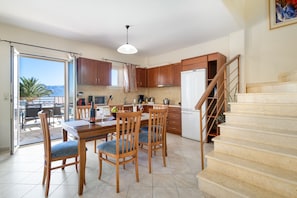 A kitchen with wooden cabinets, a dining table with chairs, a refrigerator, and a staircase leading to another level.