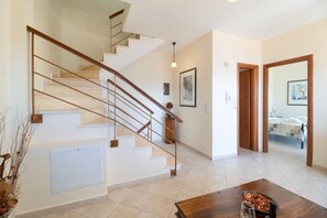 A staircase with a wooden handrail, a dining table with a bowl of fruit, and a framed picture on the wall.