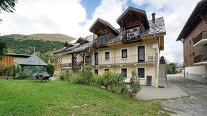 A multi-story building with balconies, a grassy yard, and a mountain backdrop. - Apartment 'Studio Cabine - Les Ecrins 2' with Mountain View and Wi-Fi (Valloire)