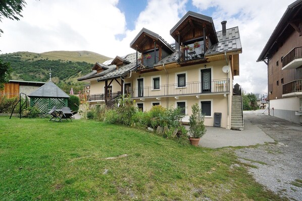 A multi-story building with balconies, a grassy yard, and a mountain backdrop.