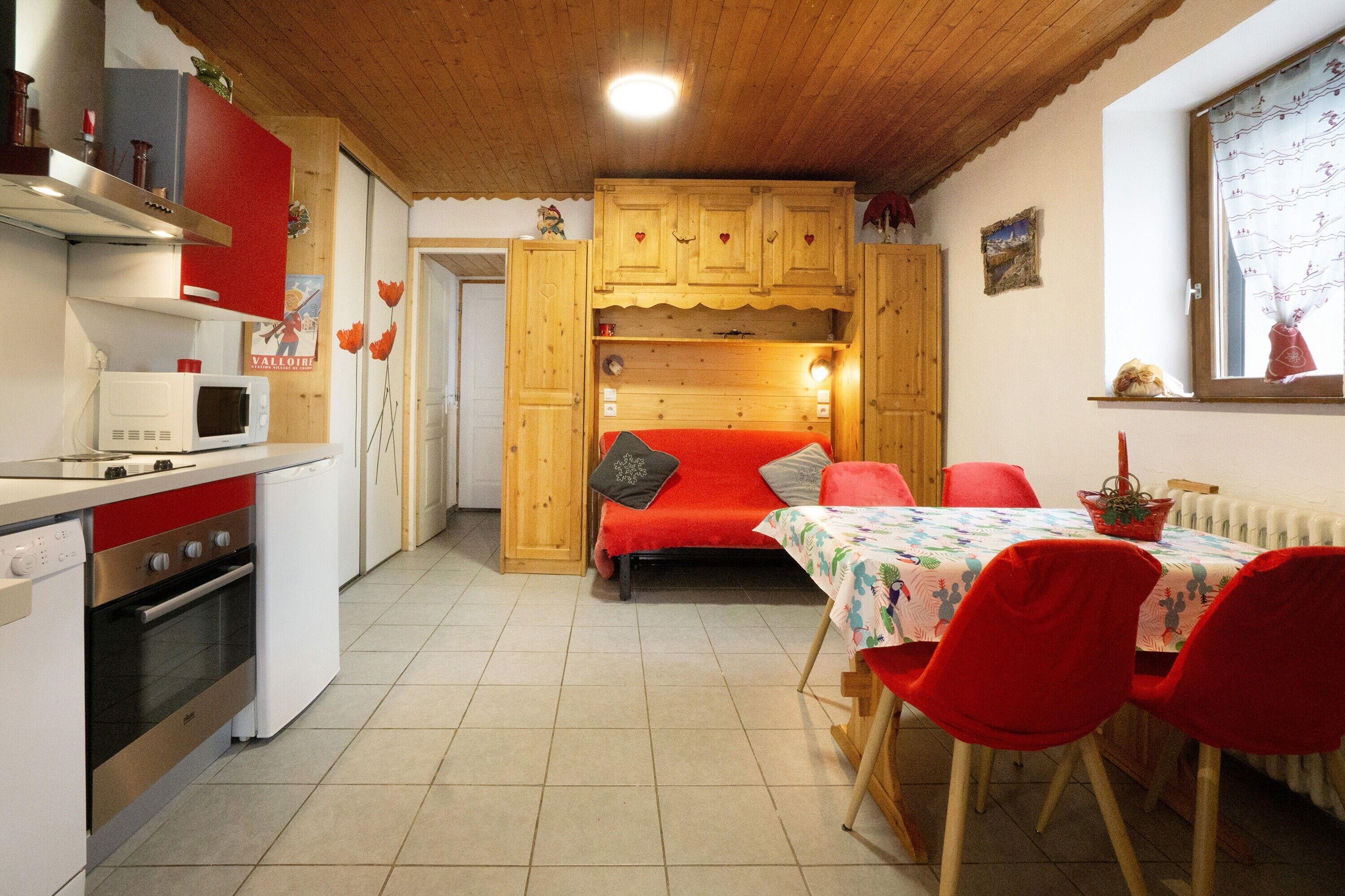 Une cuisine compacte dotée d’appareils électroménagers modernes, un coin repas avec des chaises rouges et un lit confortable avec une couverture rouge.