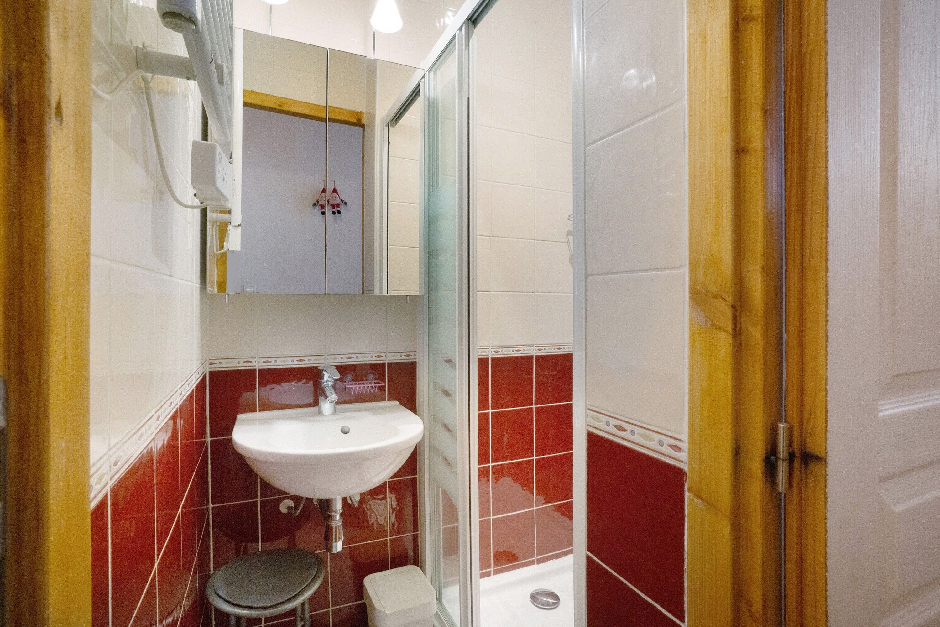A bathroom with a sink, a small stool, a shower, and a mirror.