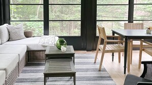 A modern living room with a large window, a ceiling fan, a sofa, a dining table, and a coffee table. - Modern Lake House on White Lake (White Lake)