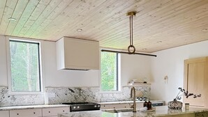 A modern kitchen with a marble island, bar stools, and a wooden ceiling. - Modern Lake House on White Lake (White Lake)