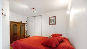 Um quarto com colcha vermelha, guarda-roupa de madeira, porta branca e quadro pendurado na parede.