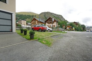 Un espace de stationnement où sont garées une voiture rouge et une voiture blanche devant un bâtiment, avec une montagne en arrière-plan.