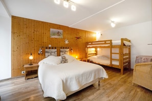 A wooden-paneled room with a bunk bed, a single bed, a nightstand with a lamp, and a wicker chair. - Apartment 'Les Ecrins 3' with Mountain View (Valloire)