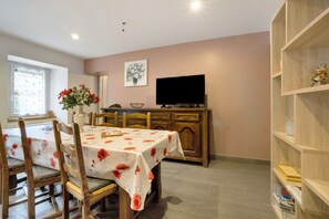 A dining area with a table set for two, a television on a stand, and a bookshelf to the right. - Apartment 'Les Ecrins 3' with Mountain View (Valloire)