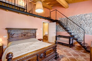 Quarto com cama de madeira, parede de pedra, escada e teto de madeira.