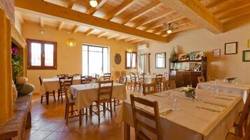 Un espace repas avec des tables et des chaises en bois, un ventilateur de plafond et un mur en briques.