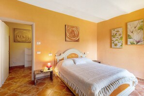 A bedroom with a bed, a bedside table with a lamp, and two wall-mounted paintings.