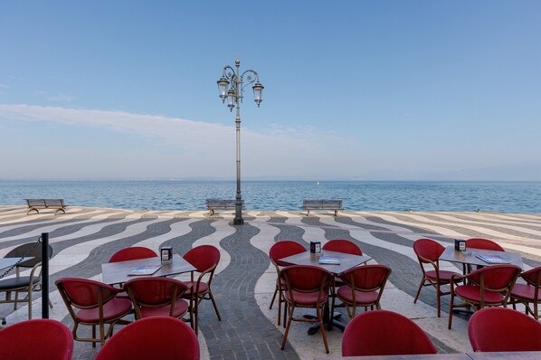 A seaside restaurant with outdoor seating, a lamp post, and a view of the sea.