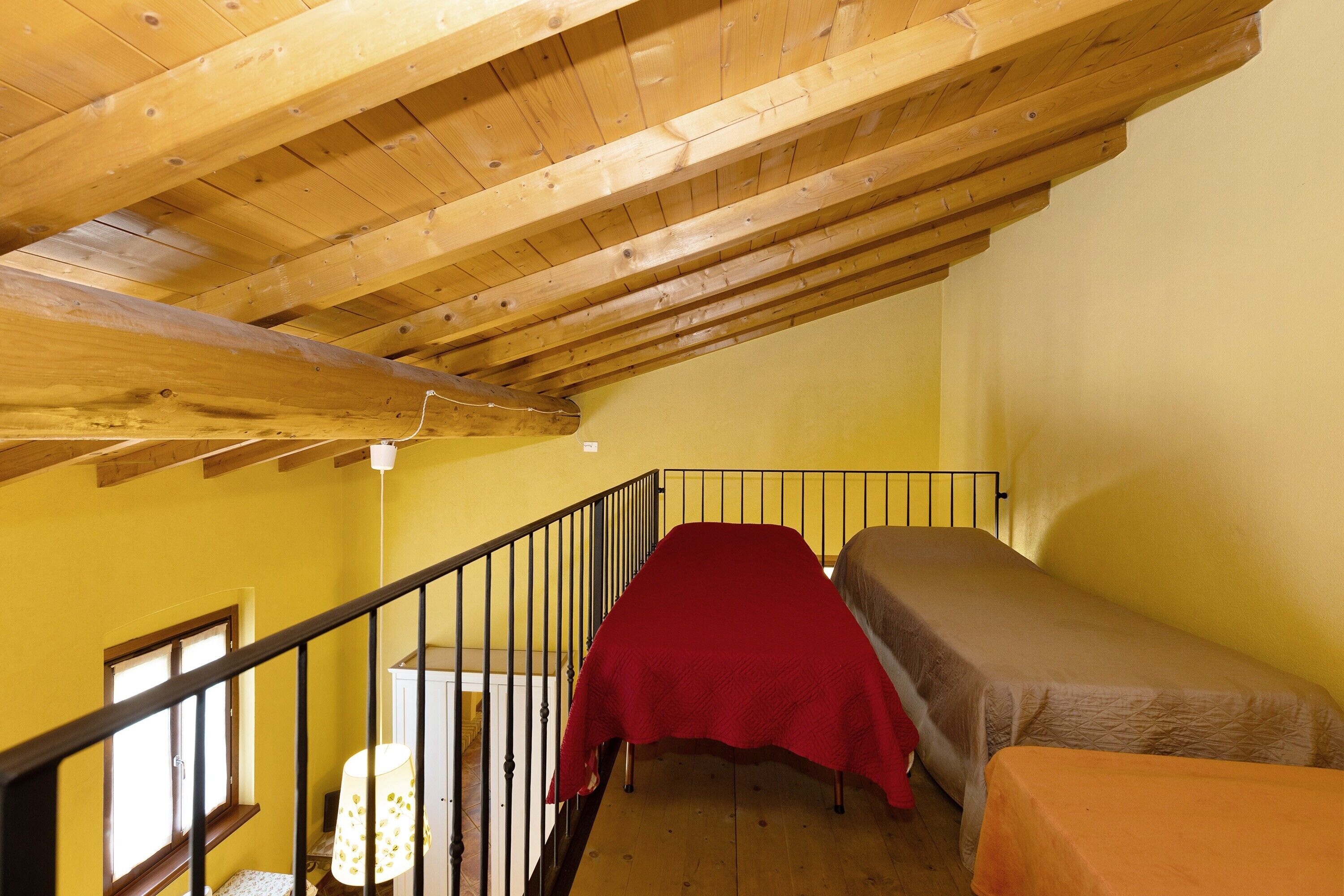 A dormitory room with wooden beams, a red bed, and a small table.