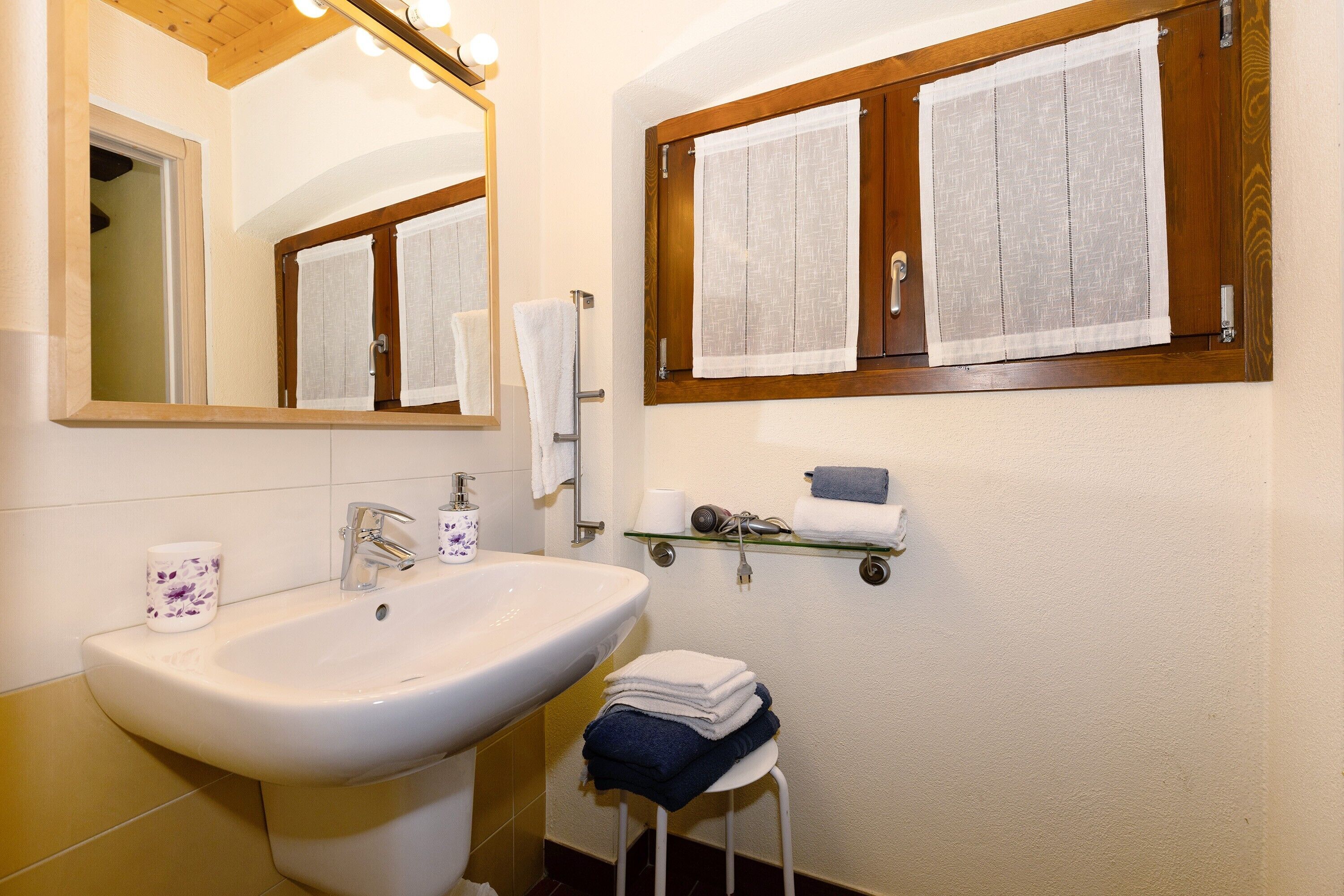 A bathroom with a sink, mirror, towel rack, and a window with curtains.