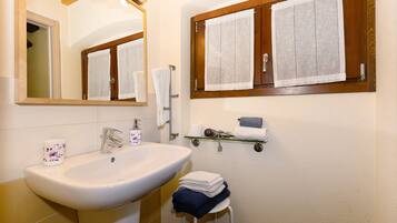 A bathroom with a sink, mirror, towel rack, and a window with curtains.