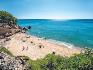 A beach with clear blue water, rocky coastline, and greenery.