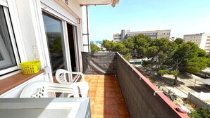 A balcony with a view of buildings and trees, a chair, a table, and a yellow basket.
