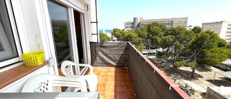 En balkon med udsigt til bygninger og træer, en stol, et bord og en gul kurv.