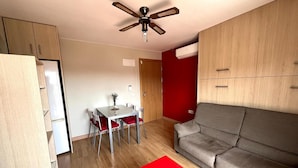 A compact living space with a dining area, a sofa, a red table, and a ceiling fan.