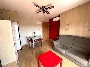 A compact living space with a dining area, a sofa, a red table, and a ceiling fan.