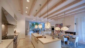 A modern kitchen with a central island, a dining area with a fireplace, and a view of the outdoors. - Villa 'Oasis Del Mar - Splendid' with Sea View, Wi-Fi and Air Conditioning (IB)