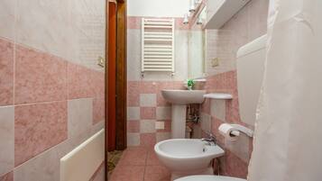 A bathroom with pink and white tiles, a white radiator, a bidet, a sink, and a toilet.