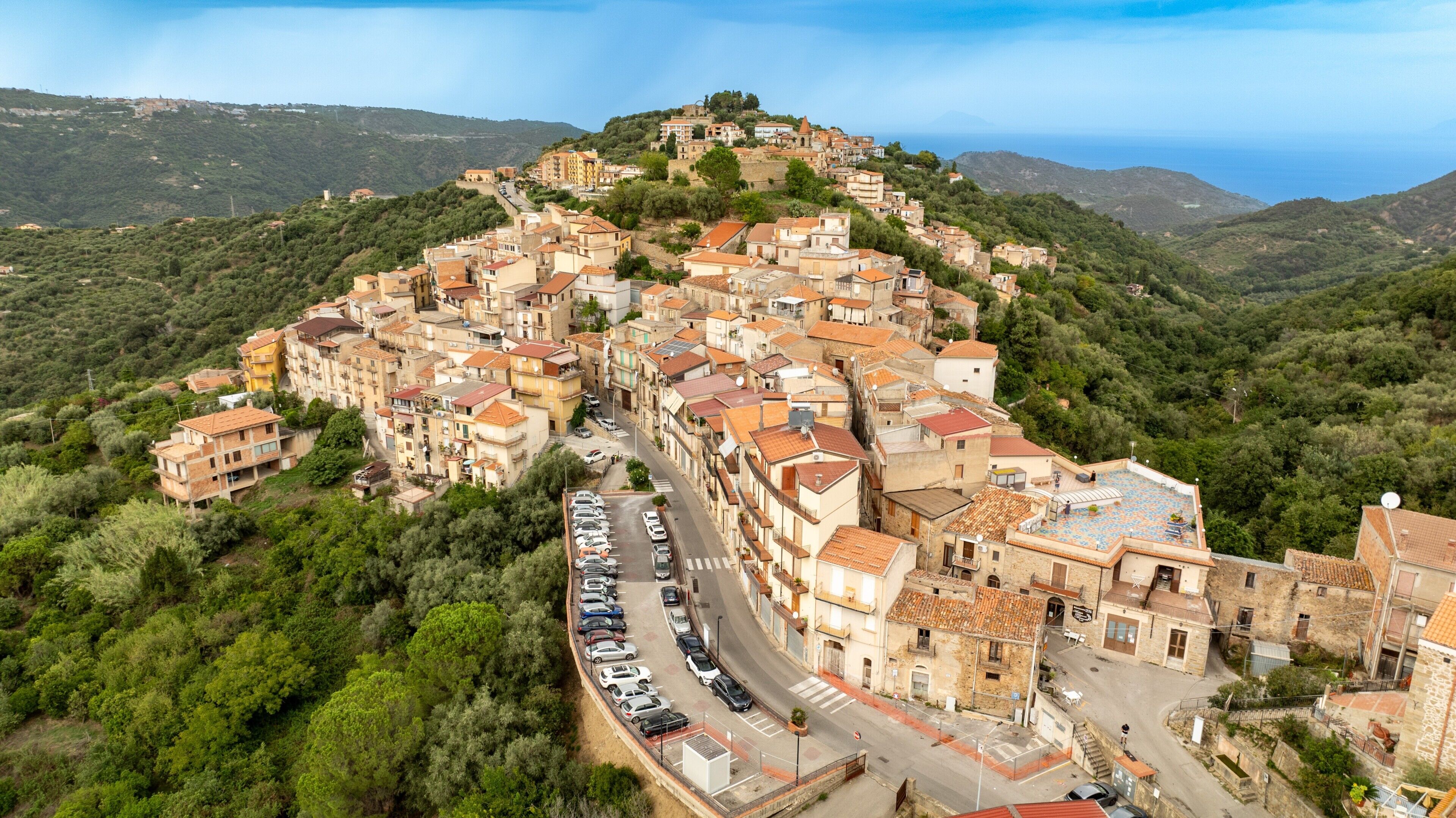 Un borgo collinare con edifici a terrazza, una strada principale e vista sul mare.