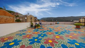 Una azotea con coloridos diseños de flores, un espacio para sentarse y vistas de edificios circundantes y colinas.