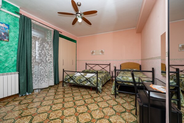 A room with two beds, a ceiling fan, a radiator, and a patterned floor.