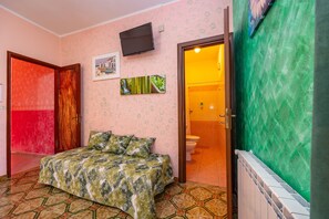 A bedroom with a bed, a television, a bathroom visible through an open door, and a radiator.