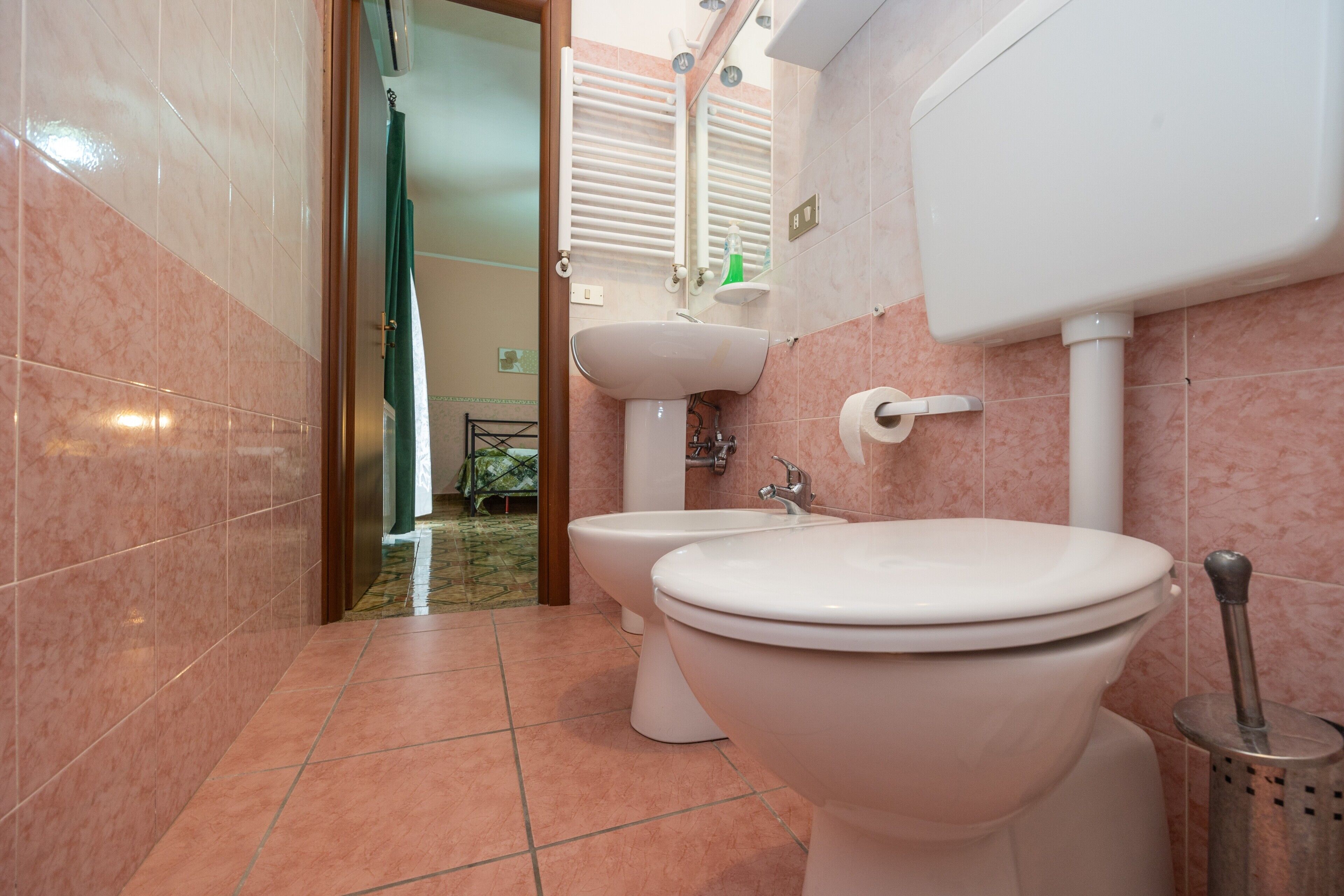 Ein Badezimmer mit Toilette, Bidet, Waschbecken und einem sichtbaren Duschbereich im Hintergrund.
