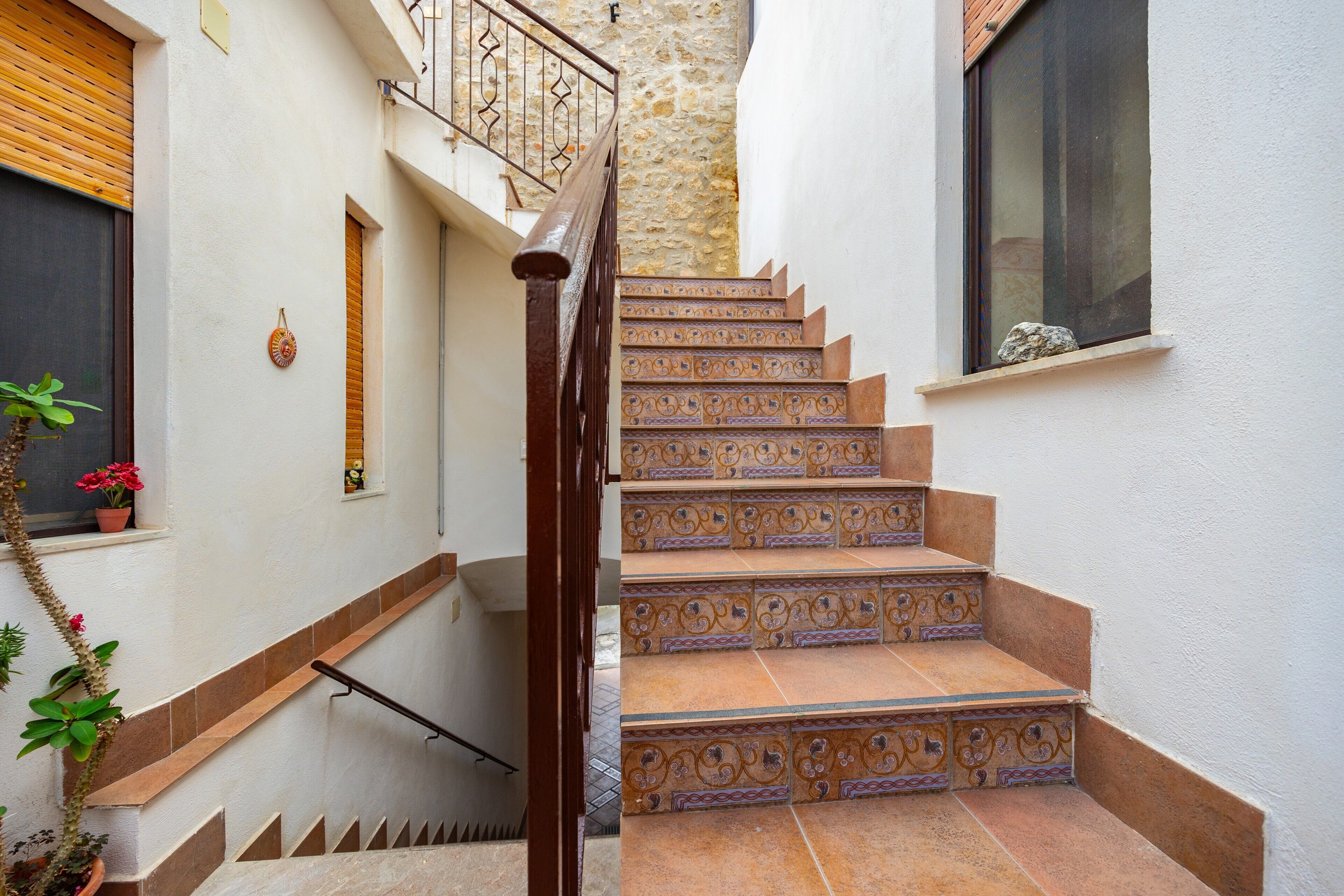 Un escalier aux marches richement décorées menant à un palier, une main courante en bois et un mur en pierre.