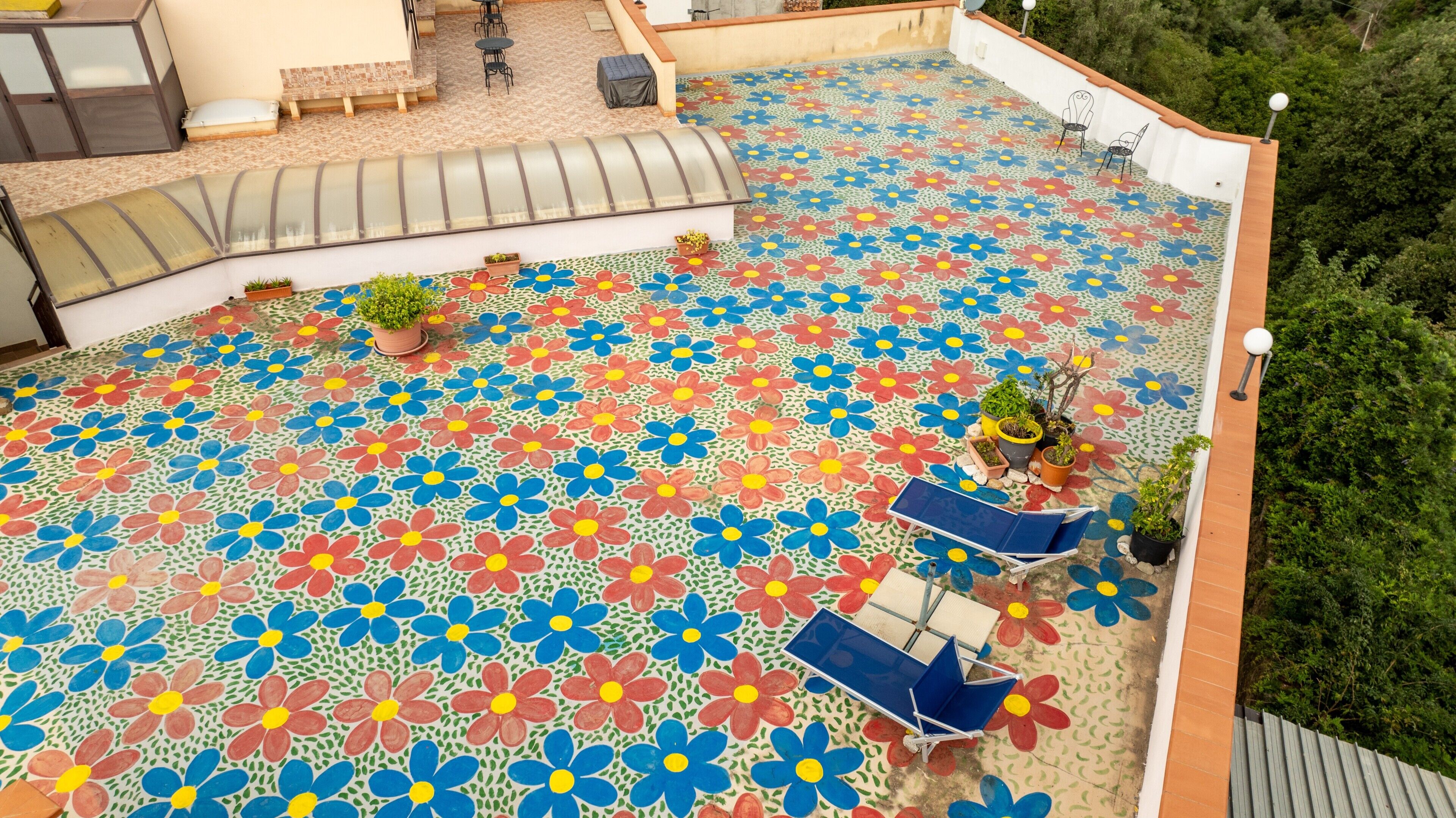 Een terras op het dak met een vloer in een kleurrijk bloemenpatroon, buitenmeubels en potplanten.