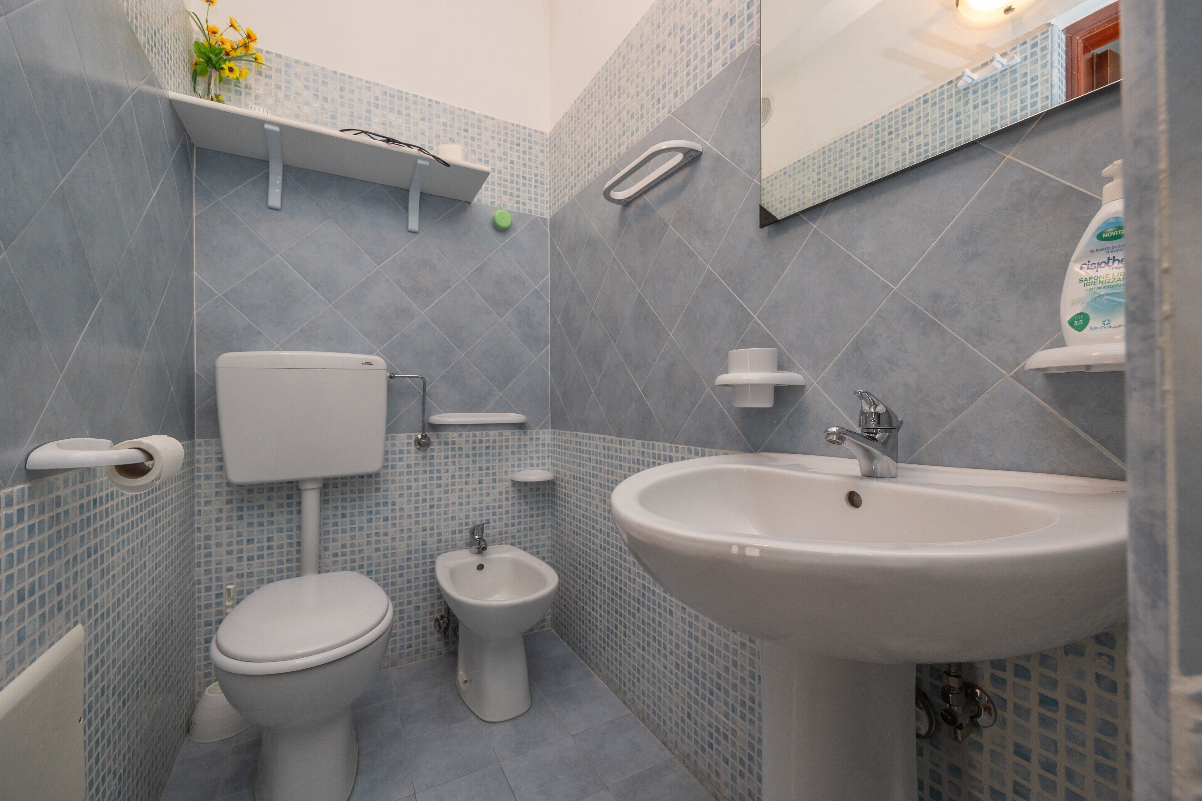 Un baño con inodoro, bidé y lavamanos, con azulejos de un patrón en azul claro.