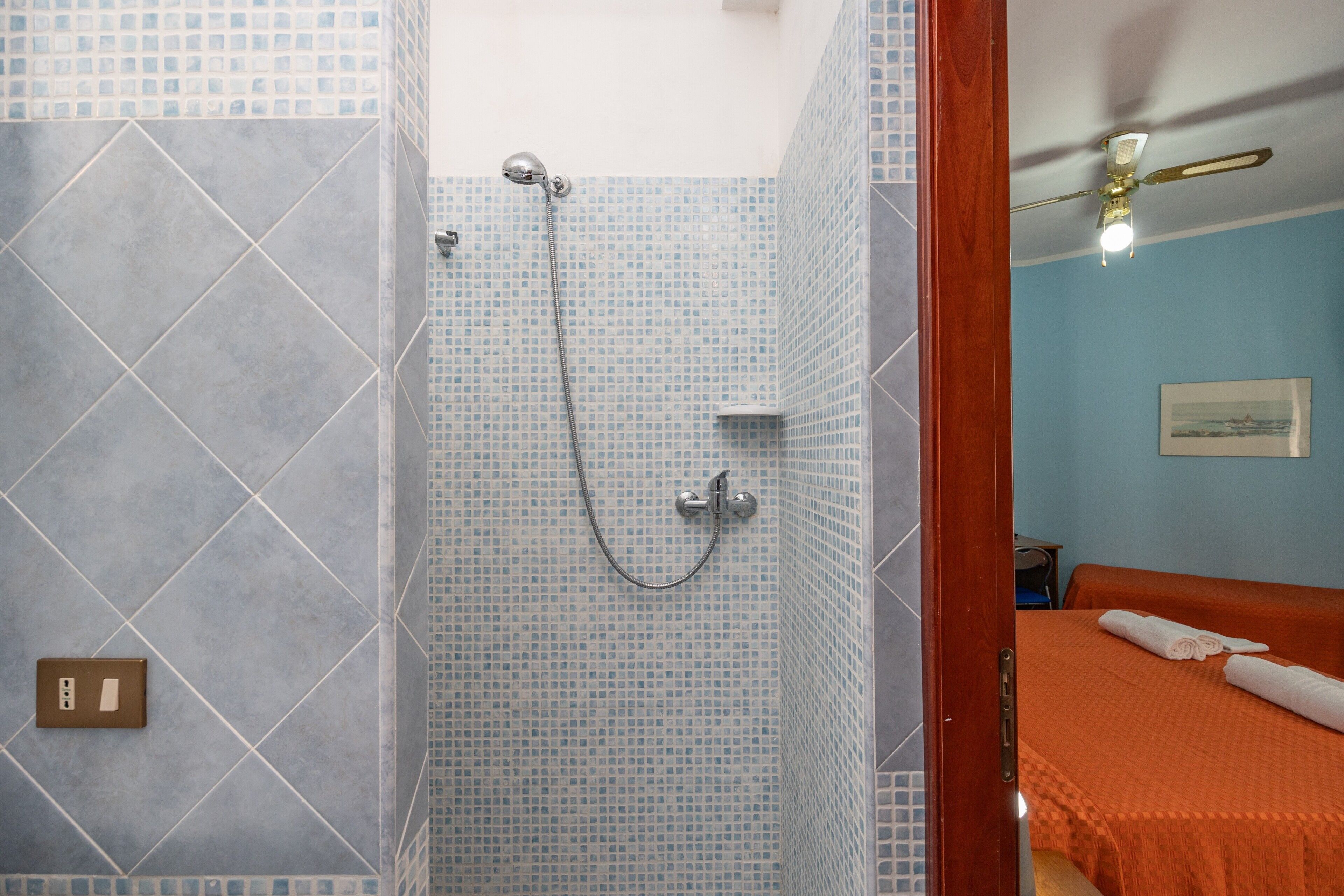 Une salle de bain avec une douche, des toilettes et un lit recouvert d’une couverture orange.