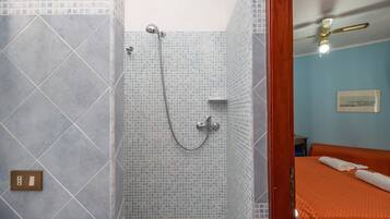 Une salle de bain avec une douche, des toilettes et un lit recouvert d’une couverture orange.