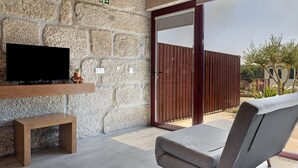 Un muro de piedra con un televisor montado, un banco, una silla de descanso y una verja de madera.