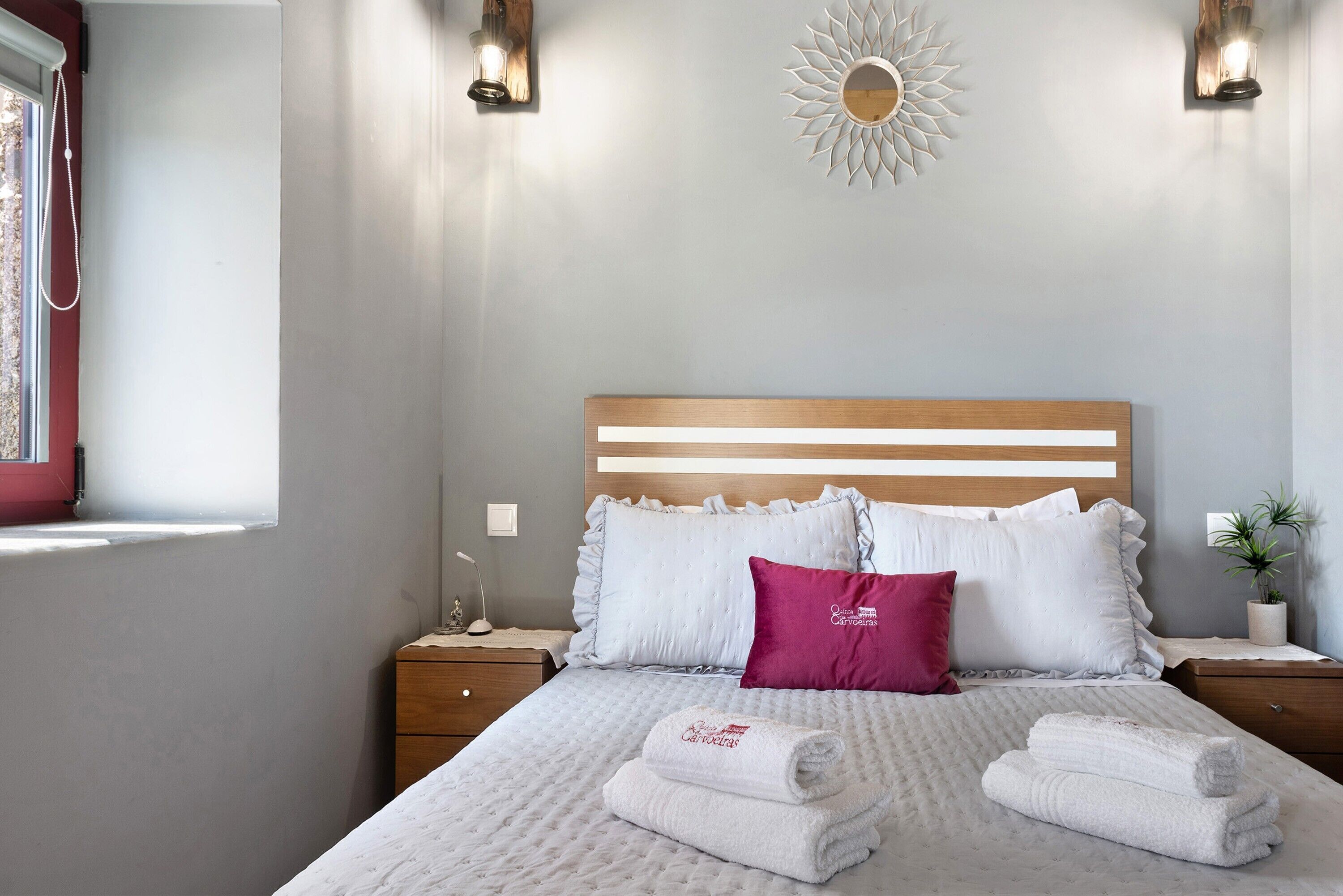 A neatly made bed with white and pink pillows, a wooden headboard, and two bedside tables with lamps.