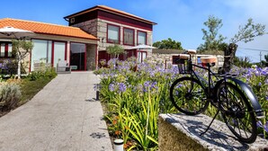 Una casa moderna de dos pisos con fachada de piedra y techo de tejas rojas, y un camino que lleva a la entrada.