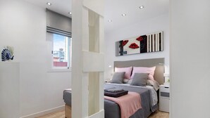 Un dormitorio con cama, mesitas de noche, ventana y vista a la ciudad.