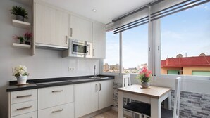 Una cocina moderna con armarios blancos, un microondas y un ventanal con vistas a un paisaje urbano.