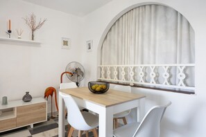 A dining area with a table, chairs, a fan, and a decorative window with a curtain.