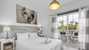 Habitación de hotel con cama, mesita de noche, lámpara, un cuadro en la pared y vistas al exterior.